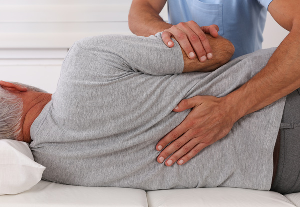 man receiving physical therapy treatment with a therapist assisting in a therapeutic exercise for back wellness and mobility improvement