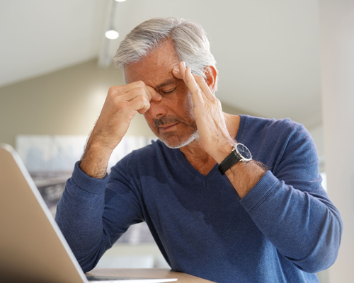 man with gray hair and beard holding his forehead while looking stressed at a laptop demonstrating work stress relief tips for three common issues