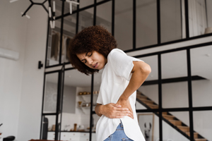 woman experiencing back pain in a modern home interior with large windows and minimalistic design focusing on health and wellness tips for eight common ailments