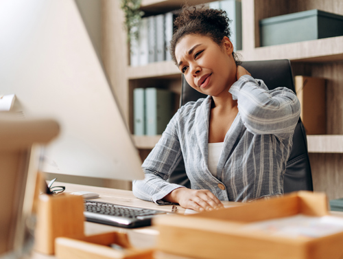 woman sitting at desk experiencing neck pain while working on computer in home office environment