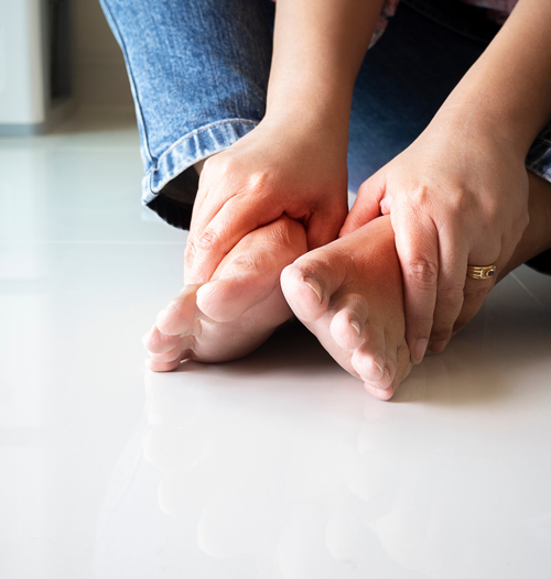 person sitting on the floor rubbing feet symptoms of foot pain and discomfort related to common issues from 13 different causes
