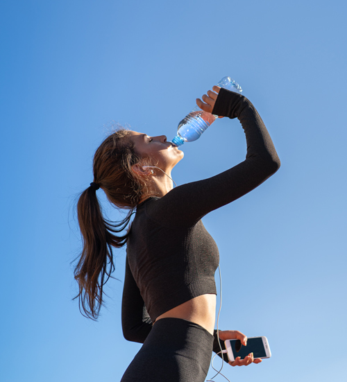 young woman drinking water outdoors during fitness routine with blue sky in background staying hydrated